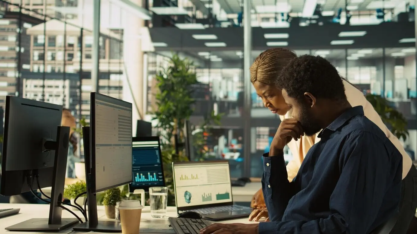 Сотрудник в офисе показывает менеджеру на ноутбуке цифры по выручке.