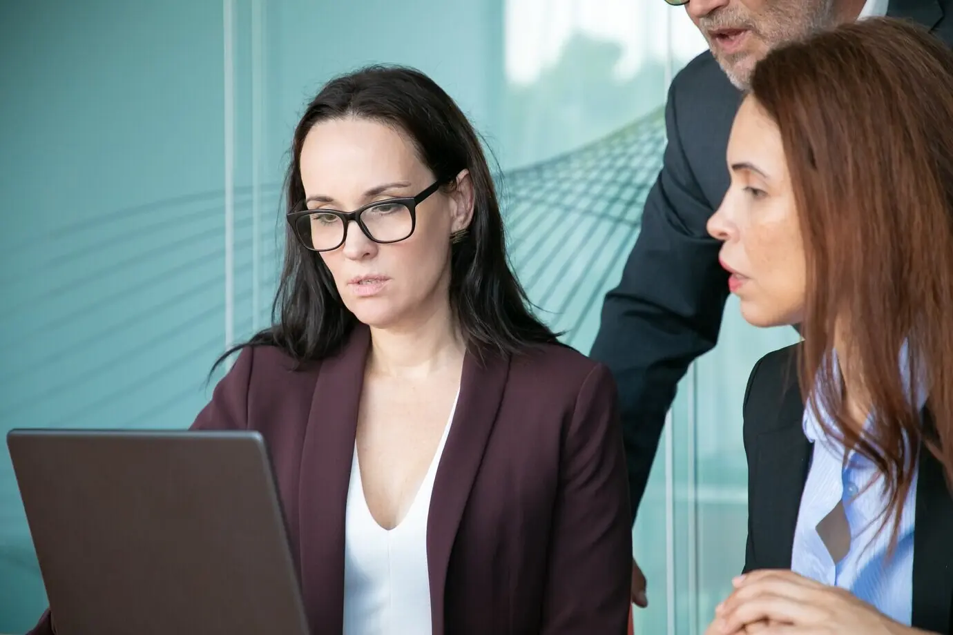 Сосредоточенные и серьезные деловые люди, сидящие и стоящие у открытого ноутбука, смотрят на экран.