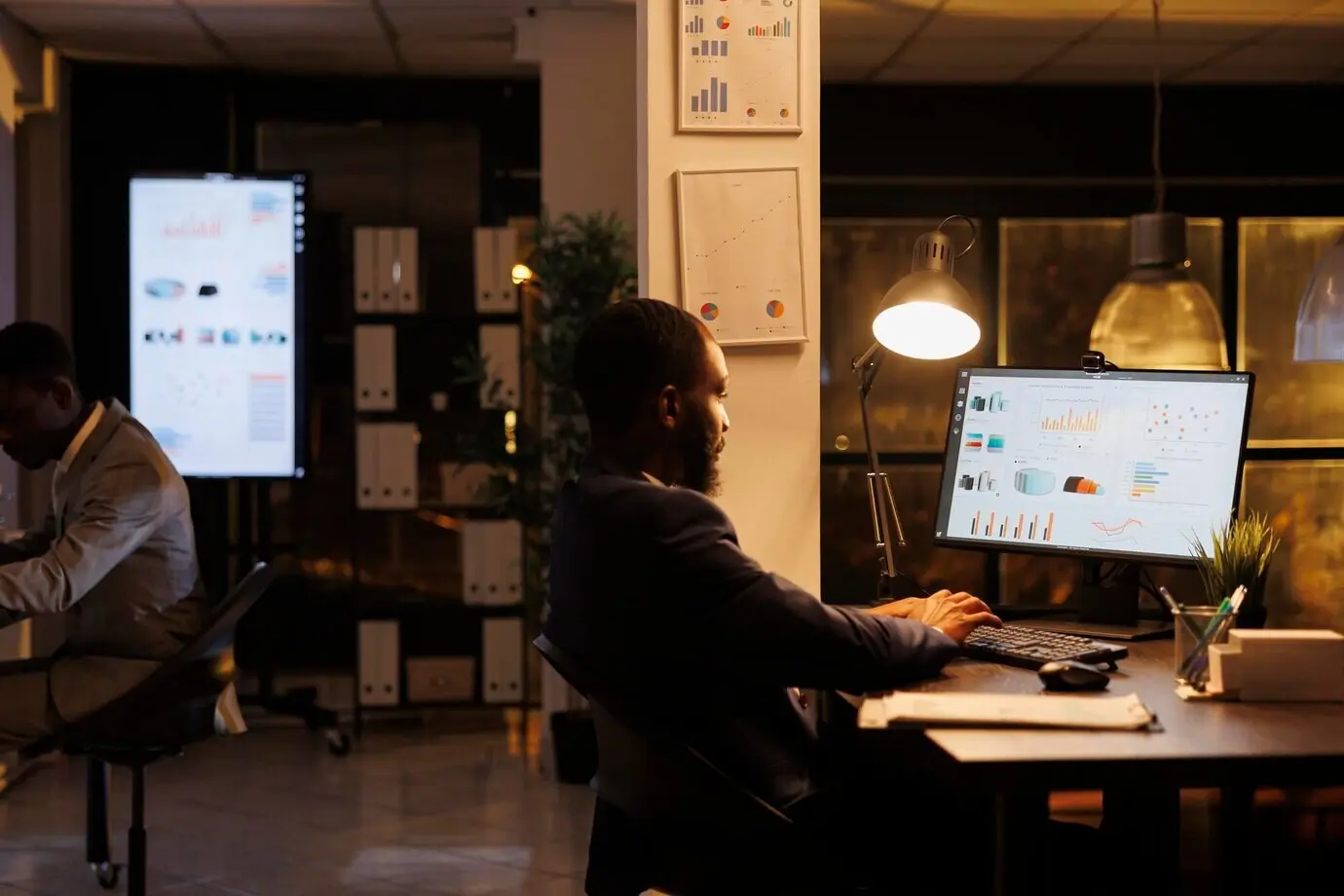 Менеджер-афроамериканец анализирует маркетинговую статистику, работая сверхурочно над стратегией проекта в офисе стартапа. Предприниматель планирует инвестиции в бизнес, чтобы помочь увеличить прибыль компании.